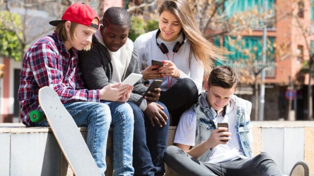 fyra ungdomar sitter på en mur och kollar deras mobiltelefoner
